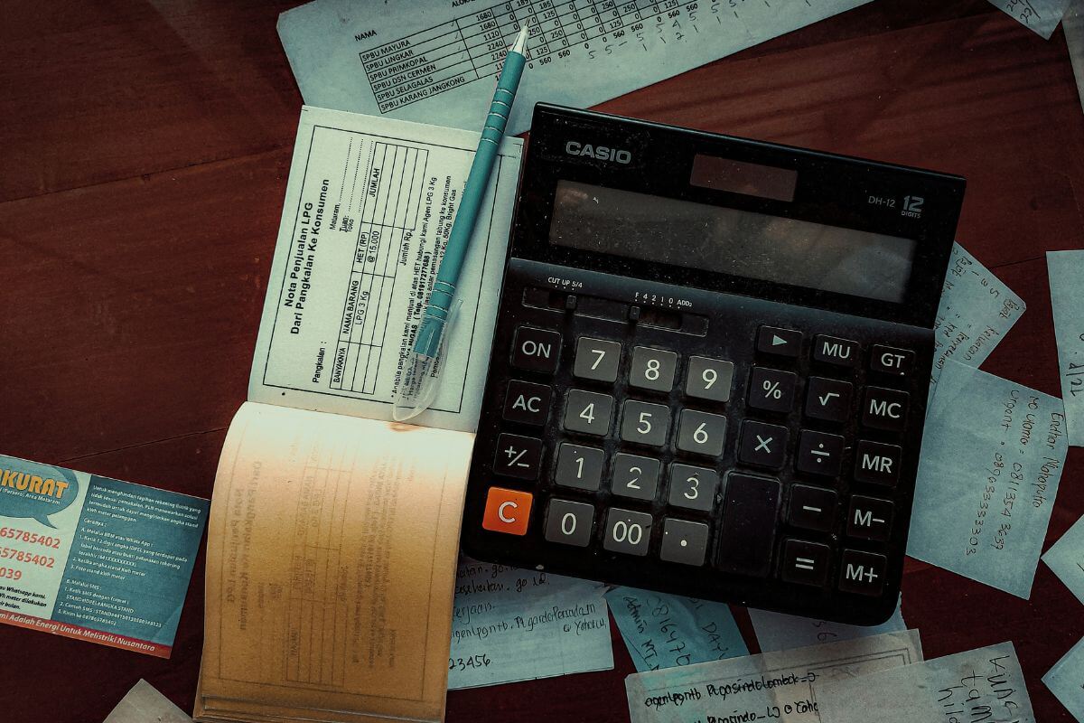 Kleinunternehmer beim Rechnung schreiben – Schreibtisch mit Taschenrechner, Notizblock, Stift und handschriftlichen Aufzeichnungen zur Rechnungsstellung.